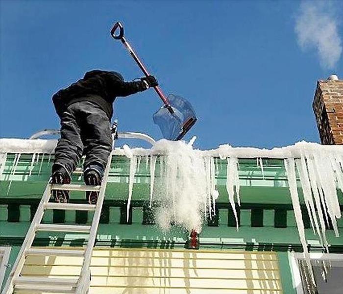 Guy on a ladder trying to scrape ice off of house.